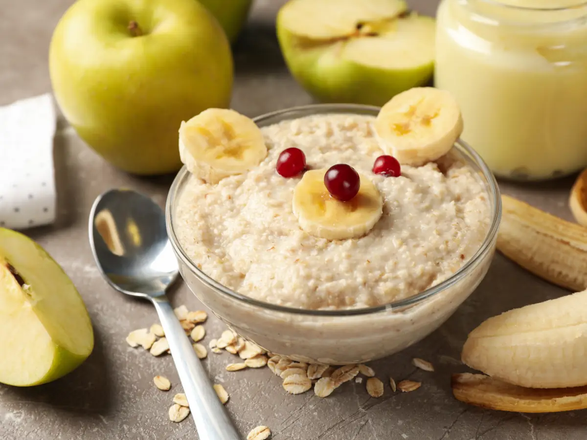 Biała miseczka na koronkowej serwecie, pełna kaszki i ozdobiona owocami w mordkę misia. Ilustracja do artykułu "5 zaskakujących sposobów na to, co można zrobić z kaszki dla dzieci w kuchni dla dorosłych"