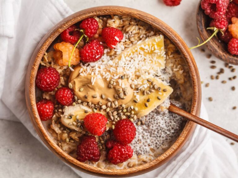 Miska widziana od góry, wypełniona płatkami owsianymi ugotowanymi i ozdobionymi owocami: malinami i brzoskwinią.