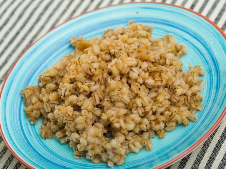 Na obrusie w biało - granatowe paski stoi turkusowy talerz z ugotowanym pęczakiem. Ilustracja do artykułu: "Czy wiesz, jak ugotować pęczak na ryby, aby zwiększyć swoje szanse na połowy?"