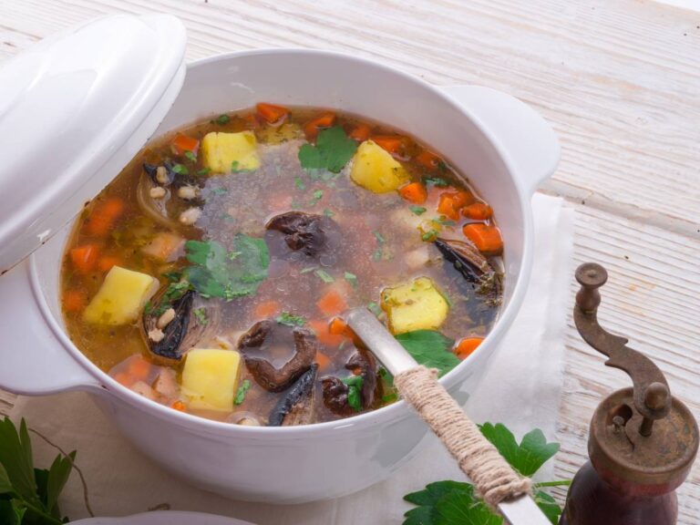 Biała miseczka z krupnikiem z grzybami i włożoną łyżką. Ilustracja do artykułu: "Rozstrzygamy odwieczny dylemat, jaka kasza na krupnik jest rzeczywiście najlepsza"