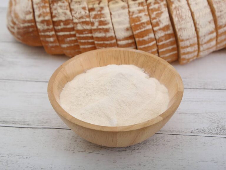 Na pierwszym planie stoi drewniana miseczka z mąką, a za nią leży chleb, pokrojony w kromki. Ilustracja do artykułu: "Odkryj, która mąka jest najzdrowsza i skąd takie wnioski"