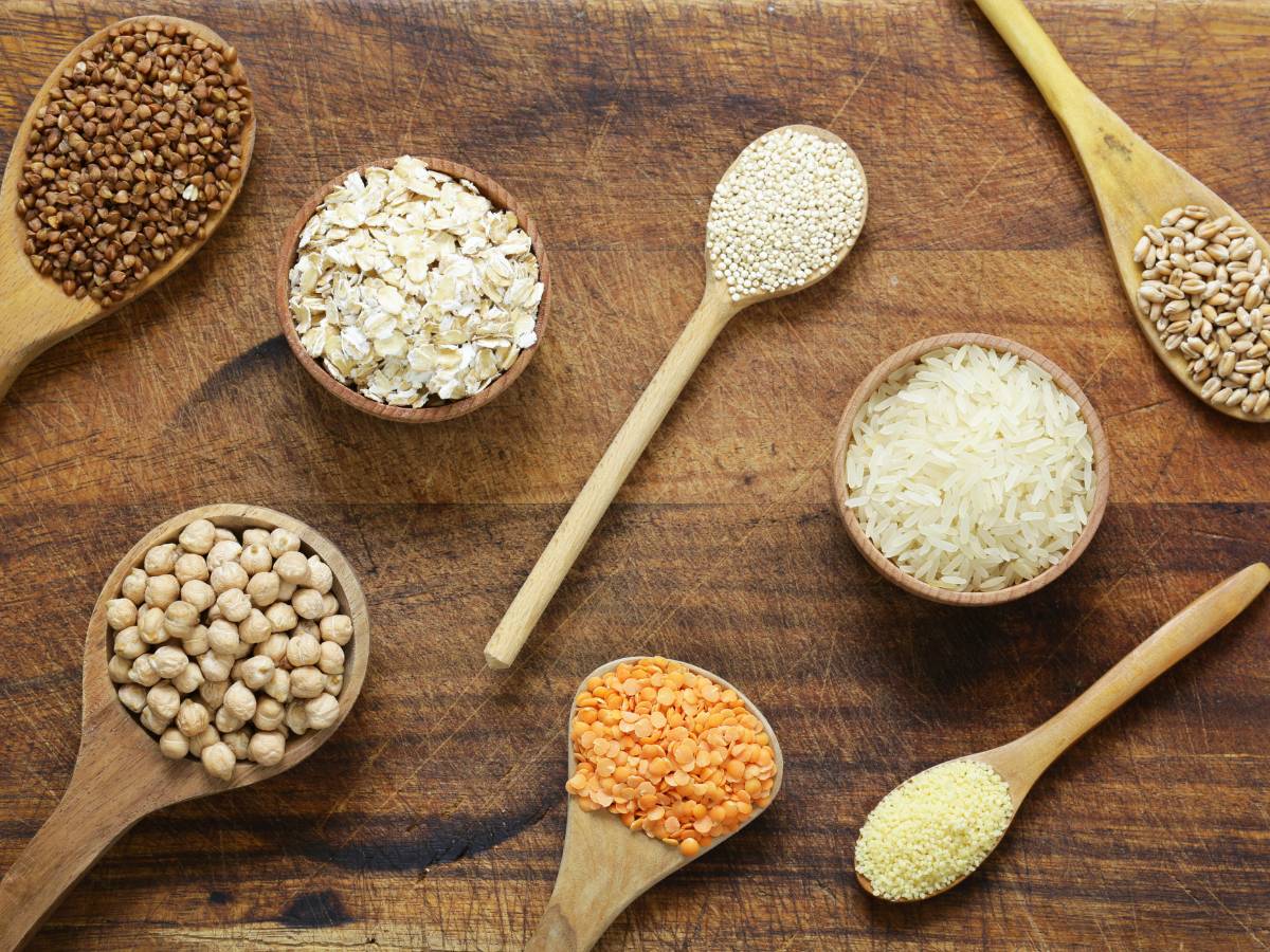 Blat stołu z ułożonymi łyżkami drewnianymi z różnymi gatunkami kaszy. Ilustracja do artykułu: "Poznaj 7 rodzajów zbóż i ich zastosowanie"