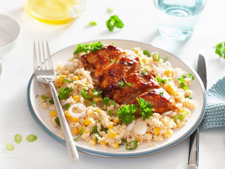 Biały talerz a kaszą, a pośrodku mięsko z sosem, po lewej leży widelec. Ilustracja do artykułu "10 inspirujących pomysłów na to, z czym jeść kuskus, dla początkujących kucharzy"