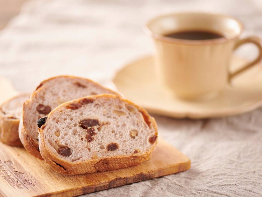 Kromki chałki z rodzynkami na desce i filiżanka kawy.