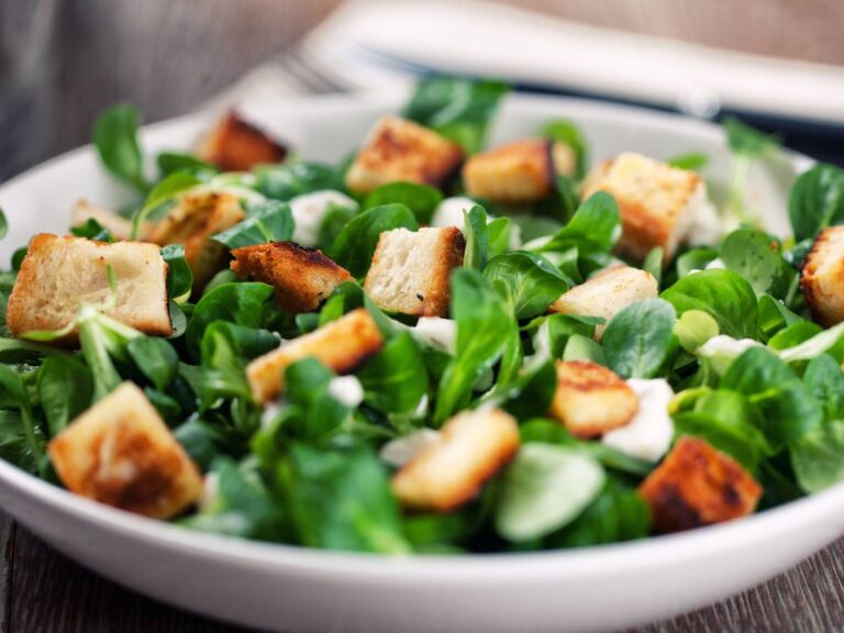 Elegancka propozycja podania sałatki Cezar na grzankach z chleba razowego na białym talerzu